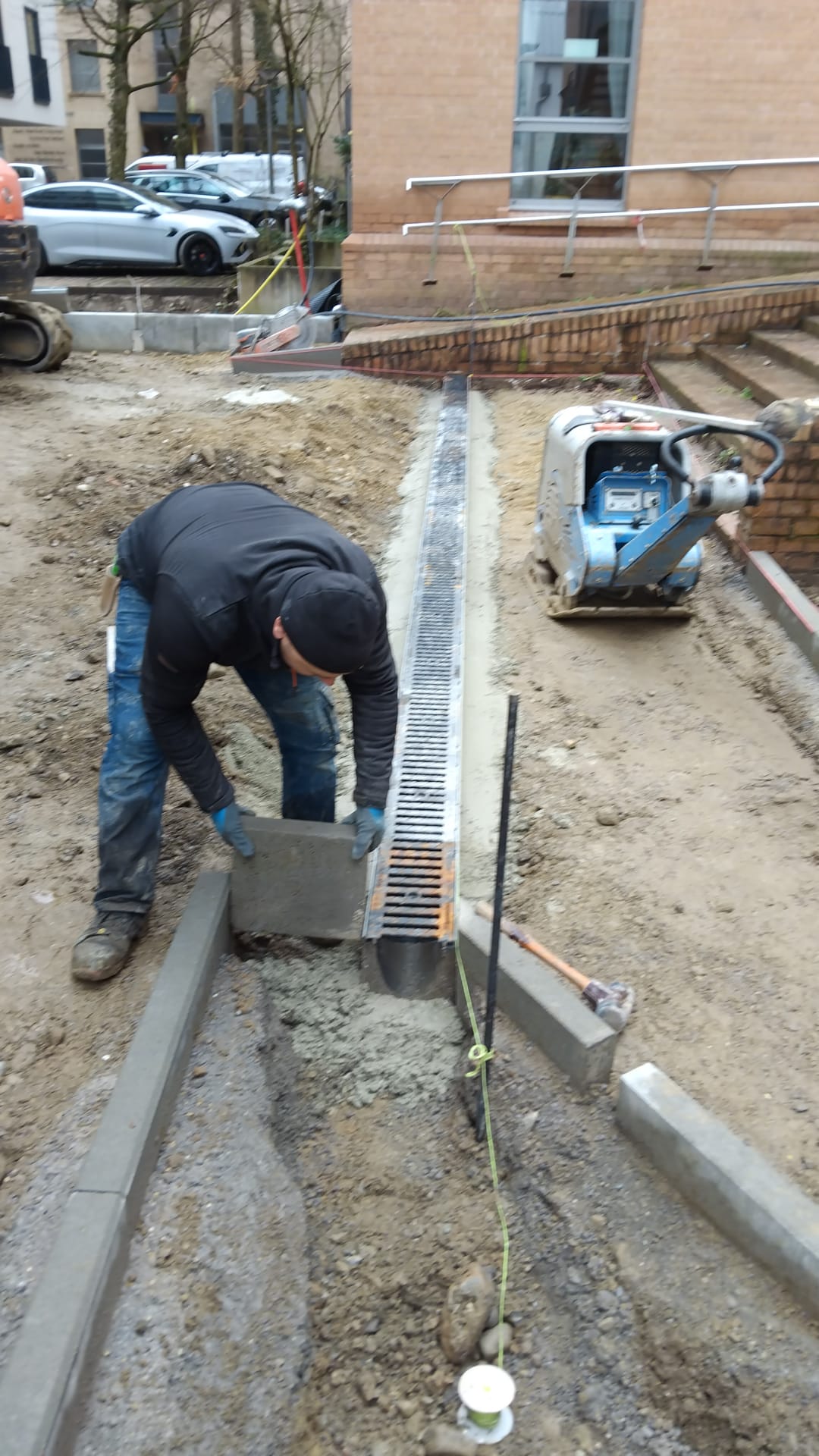 Mitarbeiter setzt Entwässerungsrinne auf einer Baustelle